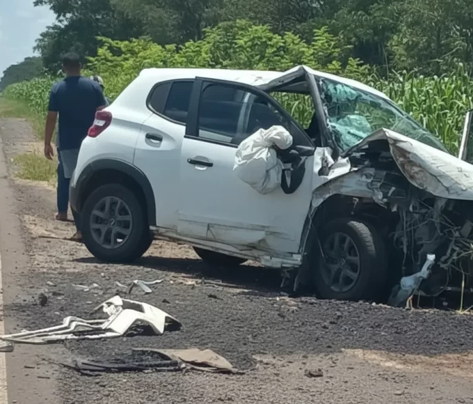 Veículo branco com a frente destruída após o grave acidente na BR-376 em Guairaçá, parado às margens da rodovia ao lado de um milharal, com pessoas ao fundo.