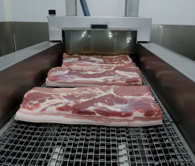 Cortes frescos de carne suína do Paraná em esteira de processamento industrial em frigorífico moderno.